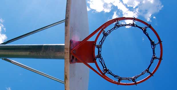 Photograph of a basketball hoop on an outdoor court, looking up towards the sky.